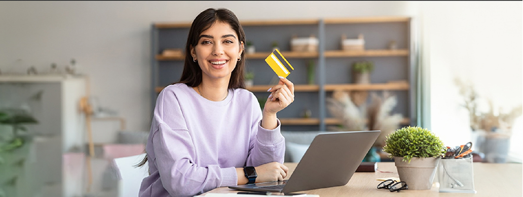 Woman holding a credit card at a desk with a laptop, suggesting ease and convenience of IndusInd Bank's instant credit cards range.